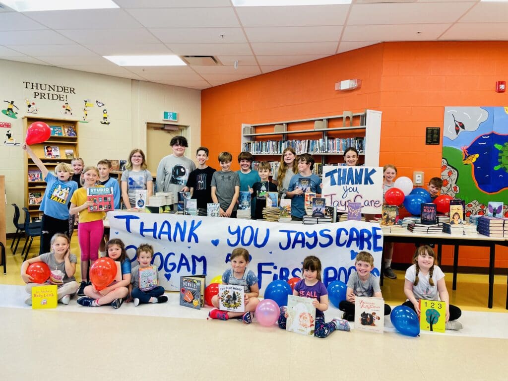 Children in a classroom showcasing a banner thanking Jays Care and First Book Canada.